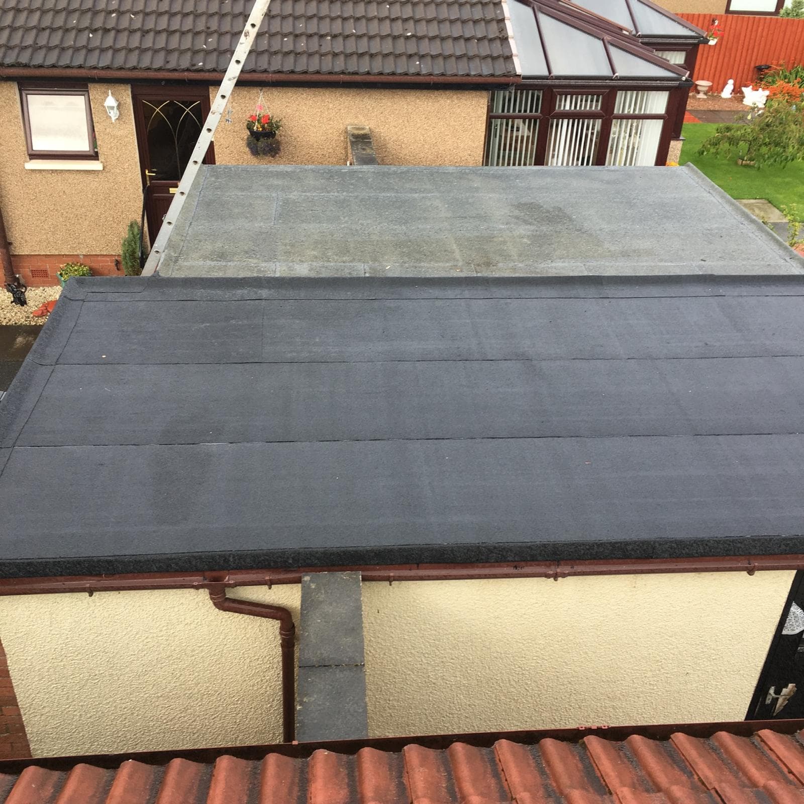 Completed flat mineral felt roof on garage extension, brown gutters, red tiles in foreground