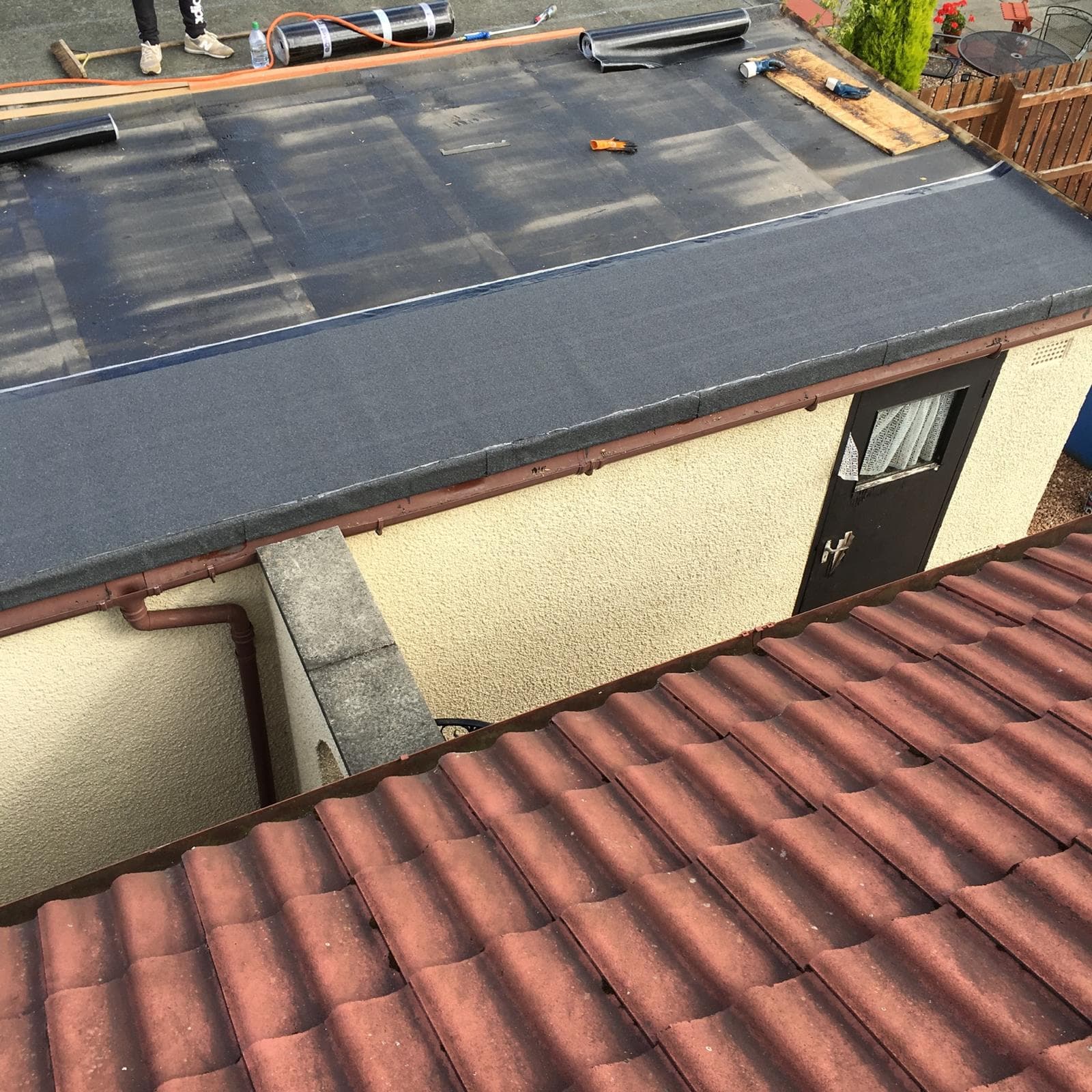 Completed flat mineral felt roof being laid on garage with rolls of felt visible