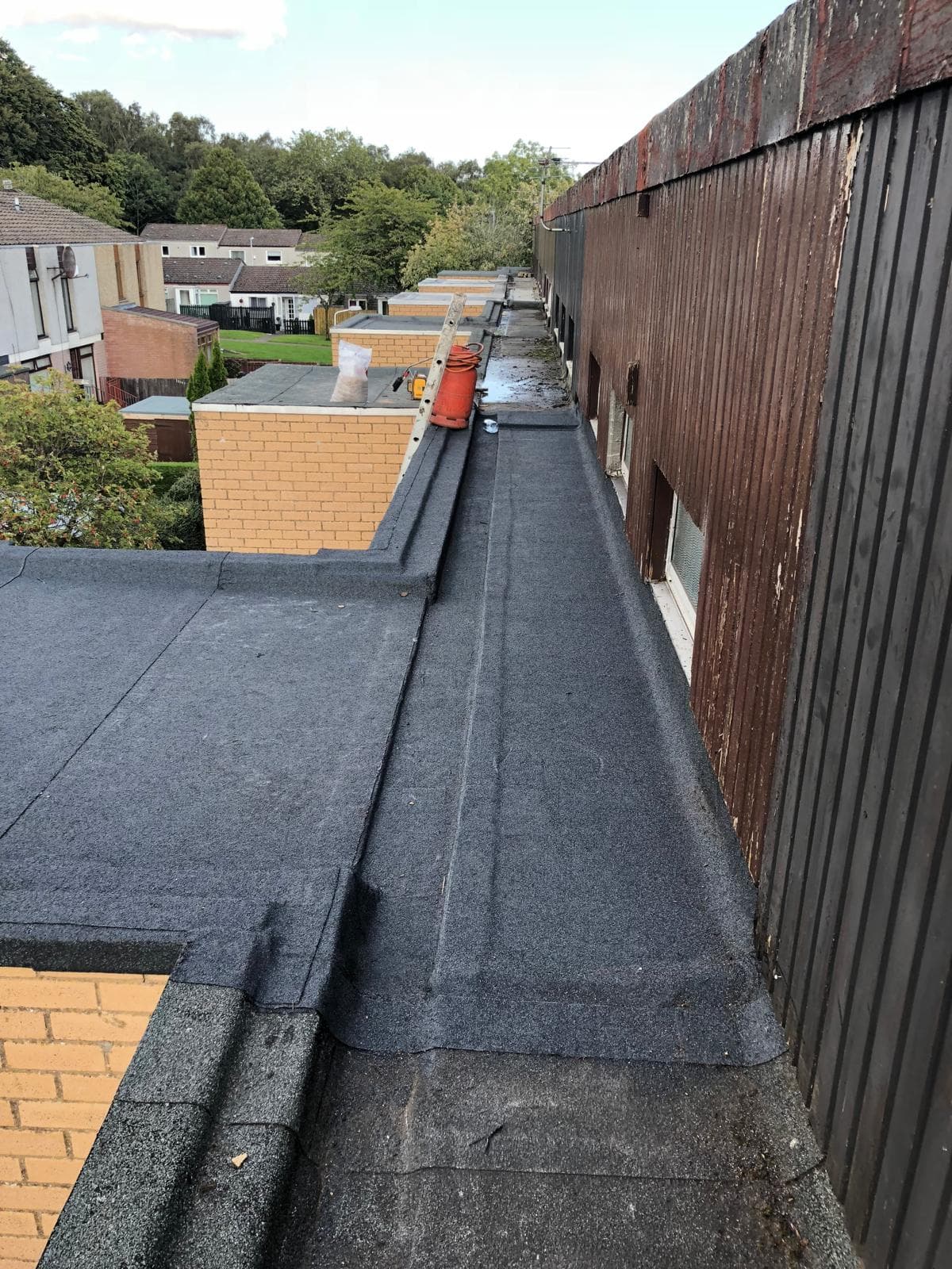 Long flat mineral felt roof being installed on a row of properties, aerial view