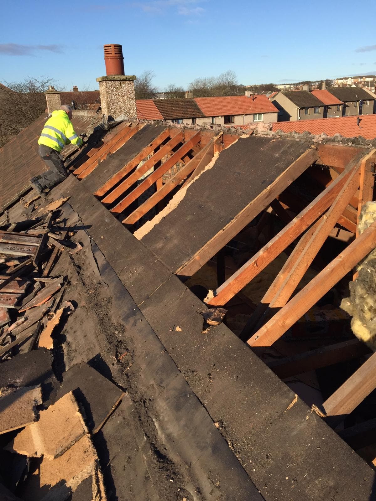 Roofer in hi-vis stripping old slates, bare rafters exposed, chimney in background