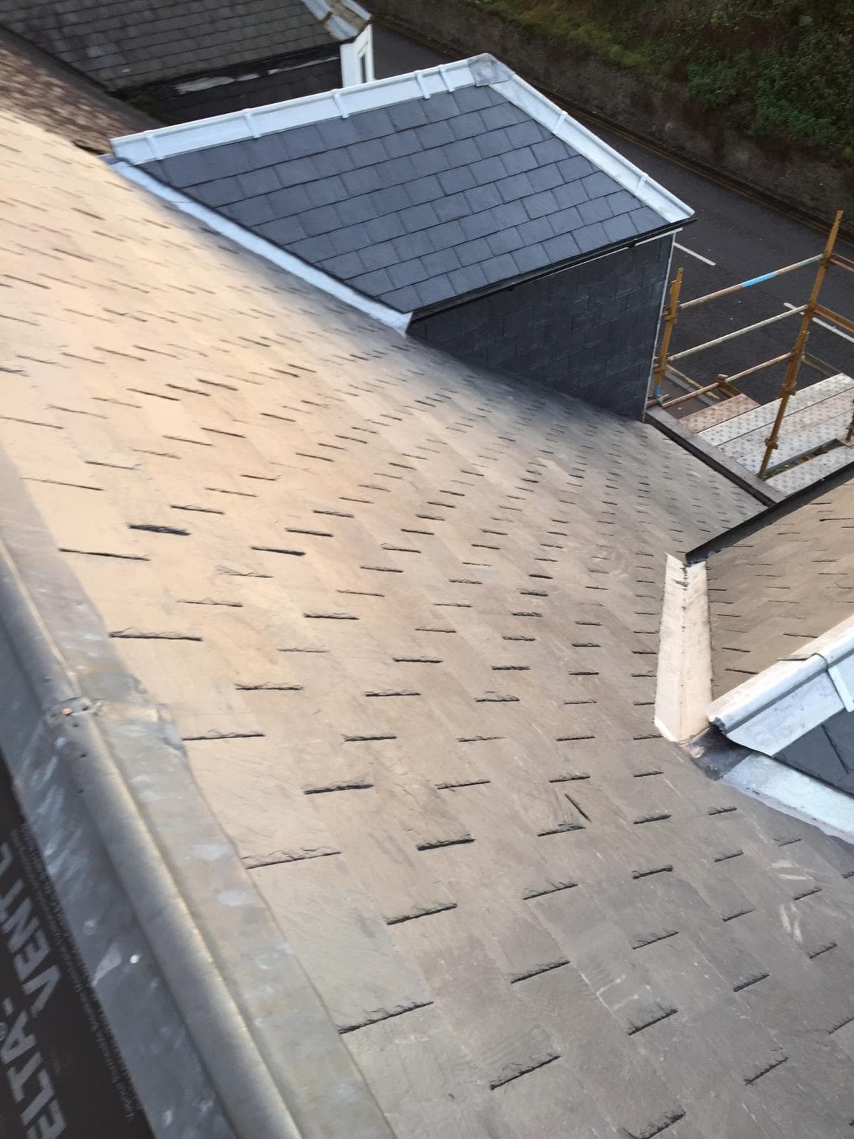 Large slate roofing project underway with scaffold, new dark slates being laid