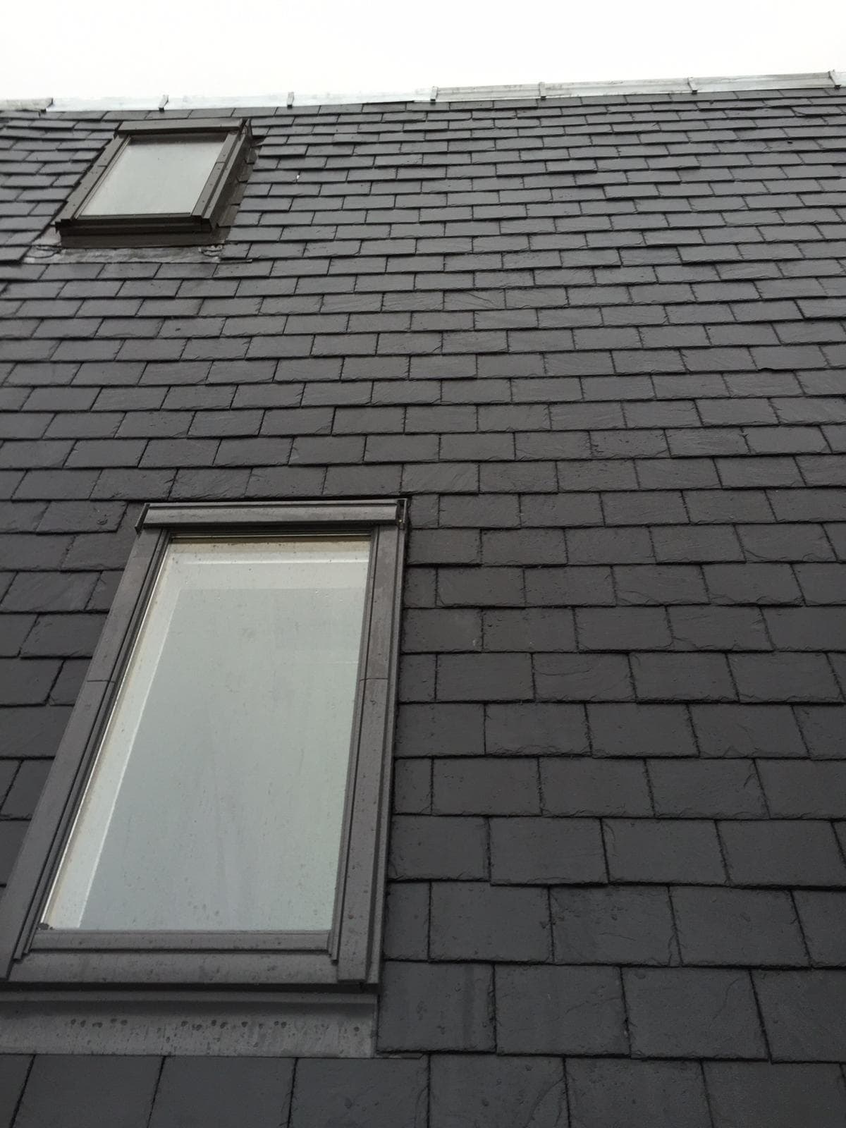 Two Velux roof windows installed in a dark slate roof at different levels