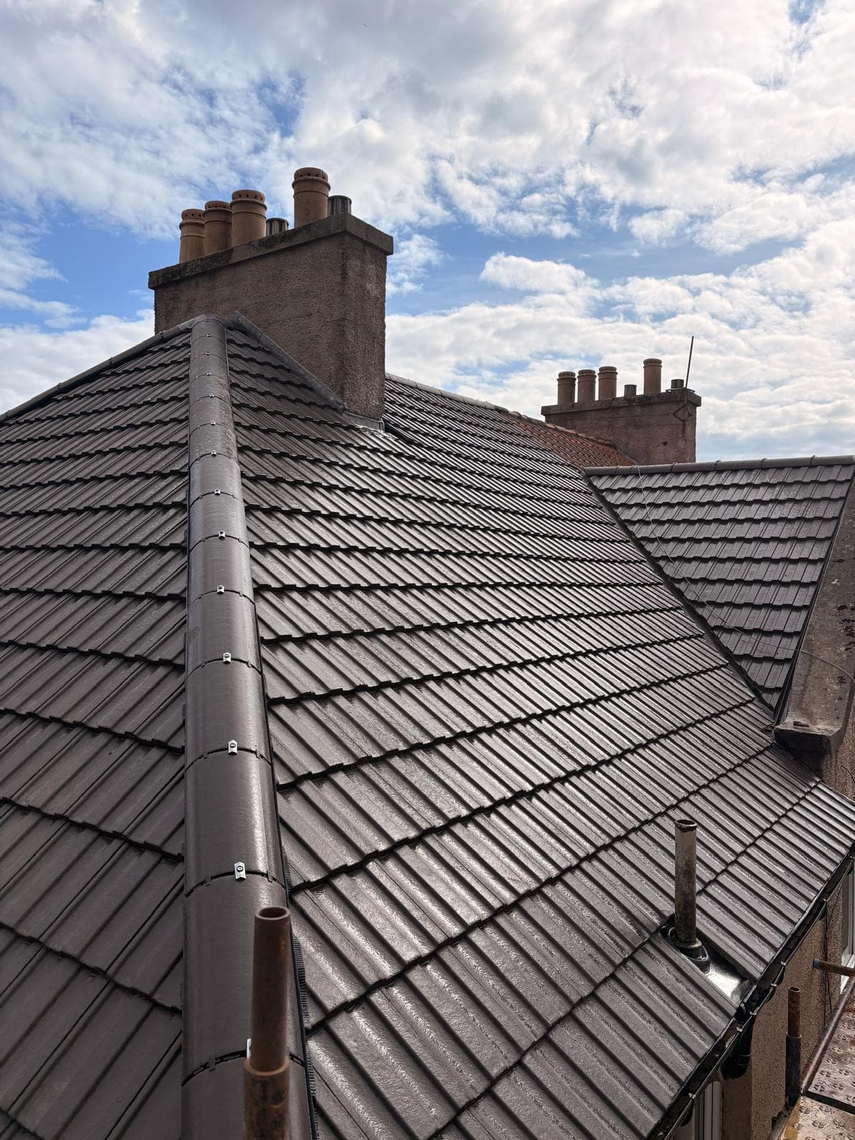 Completed dark grey tiled roof with traditional chimney stacks and clay pots against a blue sky in Scotland